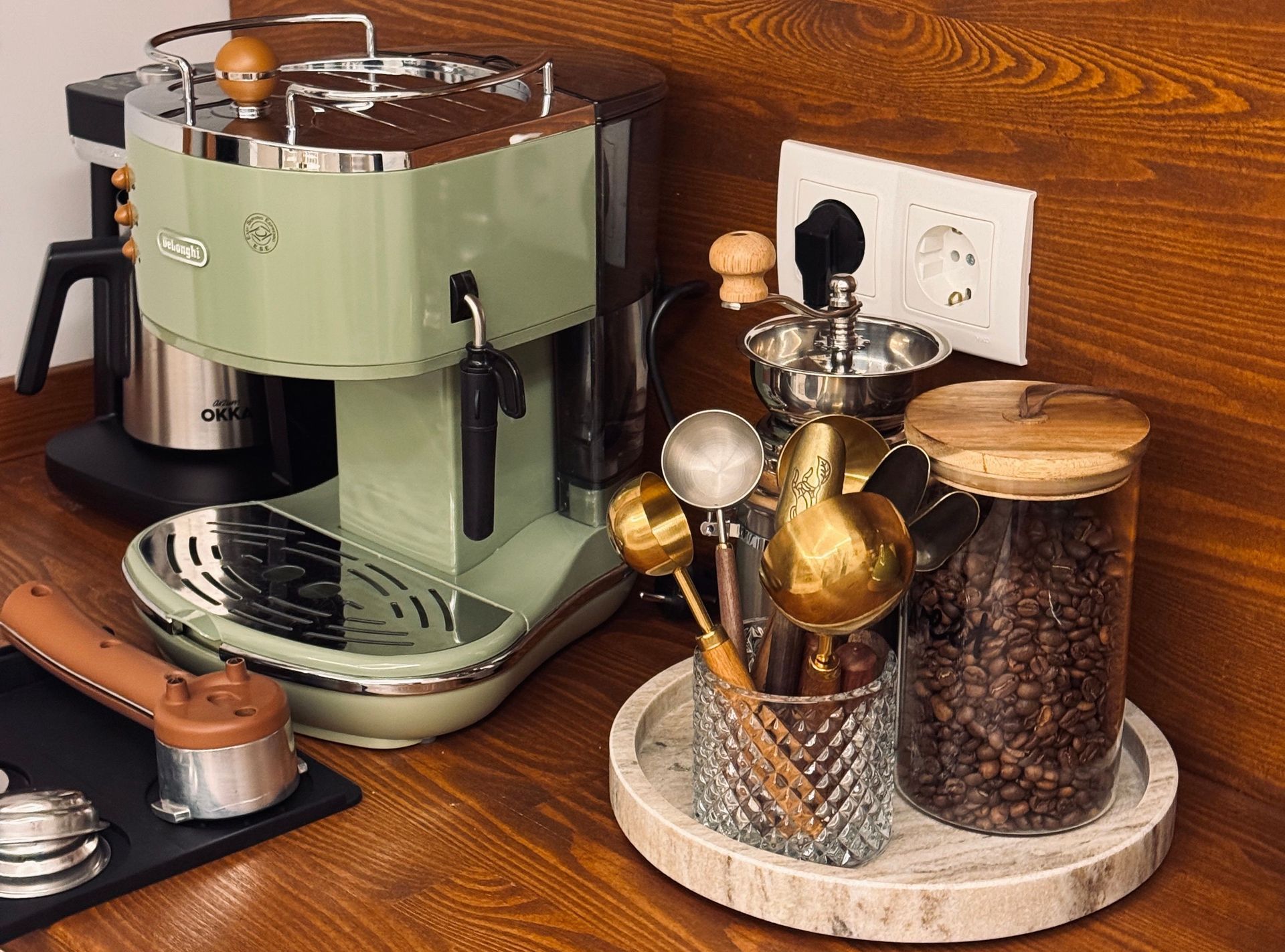 A green espresso machine sitting on a counter next to a glass jar of coffee beans and golden measuring scoops.