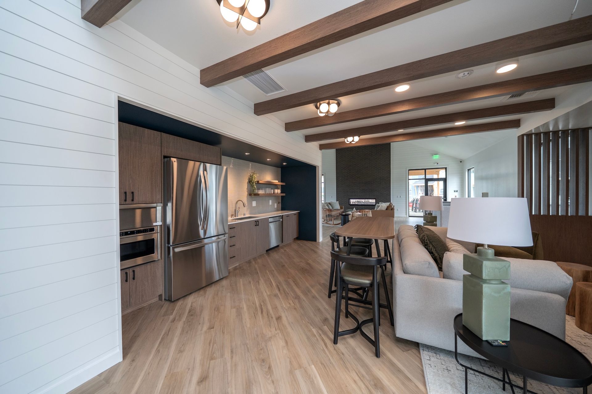 Modern lounge area with kitchen and seating, including a fridge, cabinets, and a sofa.