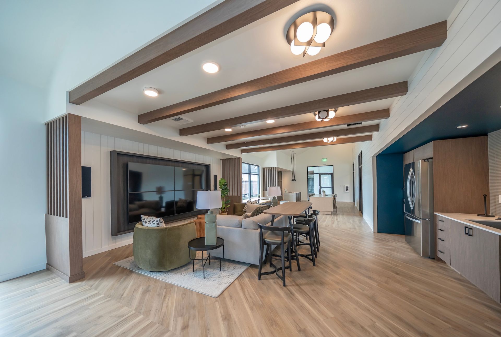 Living room with a large TV, beige flooring, and wooden beams.