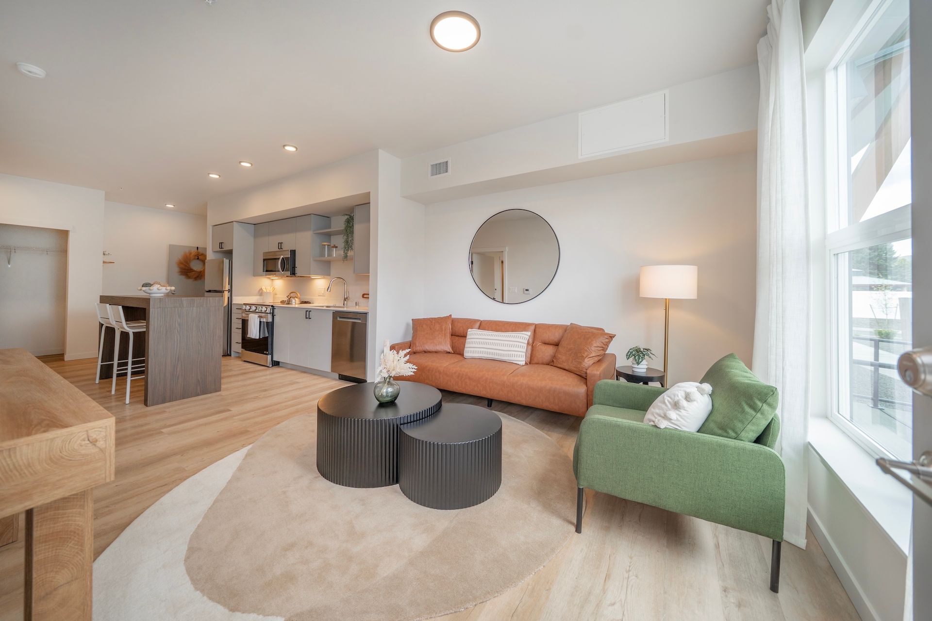 Modern living room with orange couch, green chair, and round coffee tables on a rug.