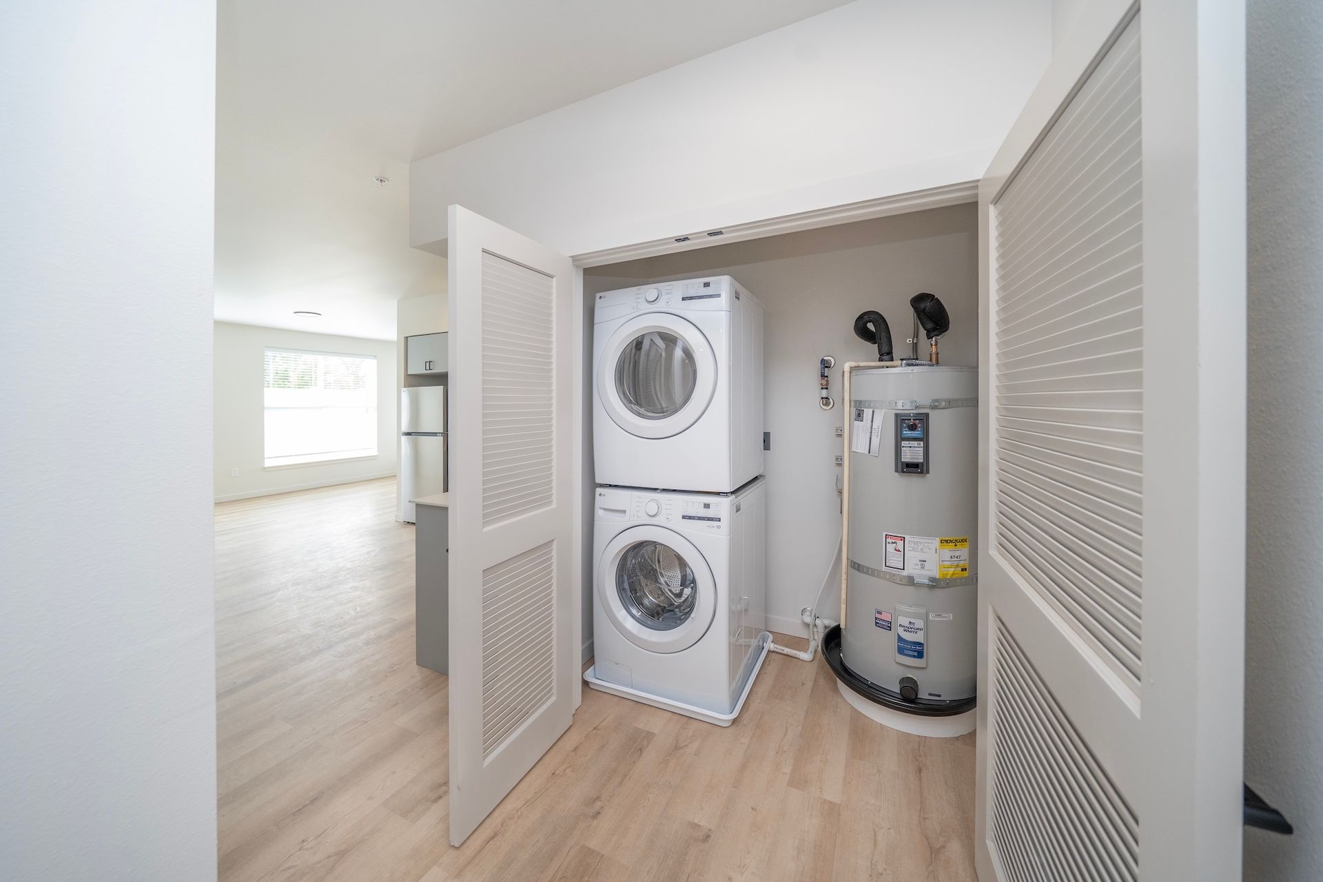 A laundry room with a stacked washer/dryer, a water heater, and wooden doors.
