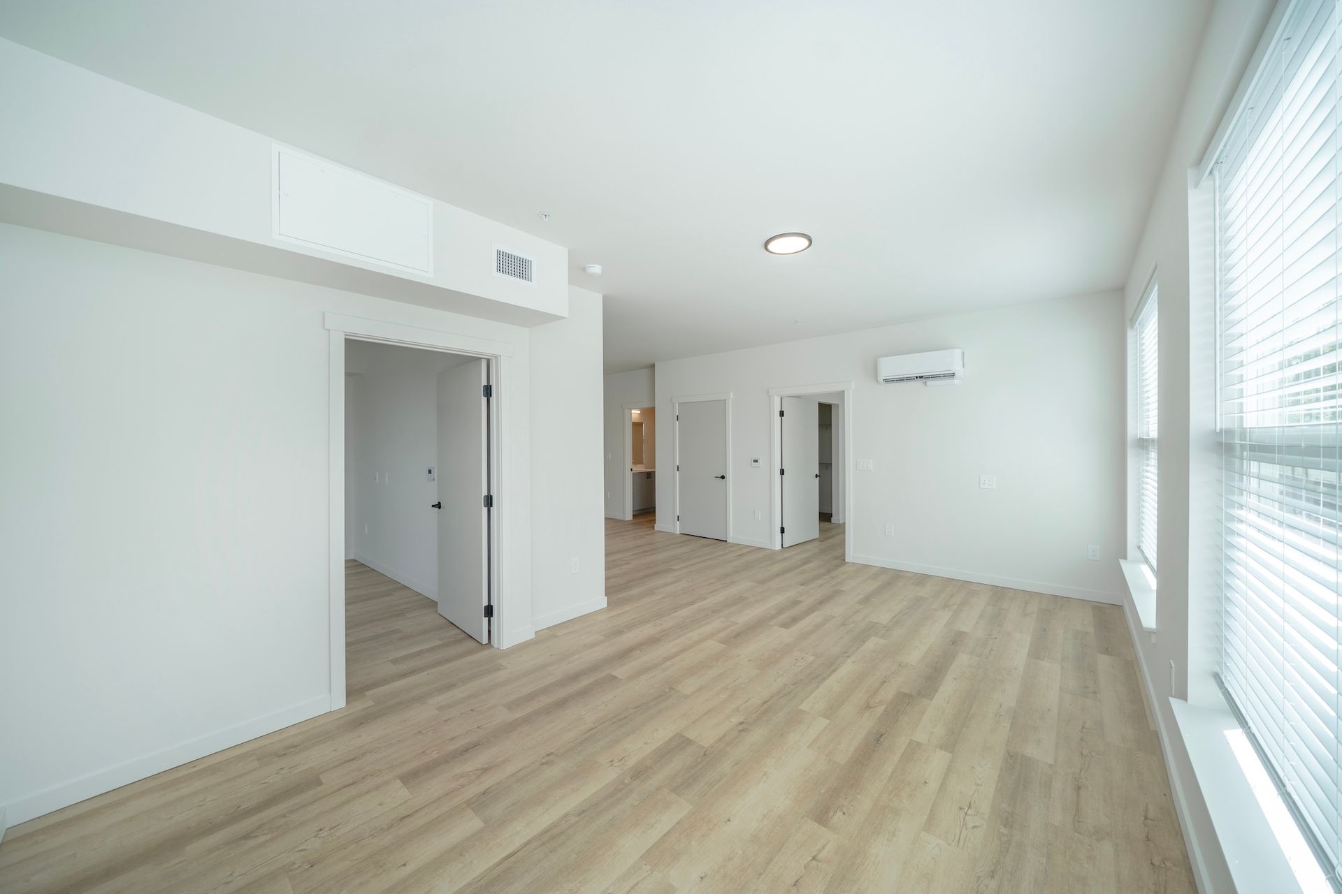 Empty room with light wood floors, white walls, and two closed doors.