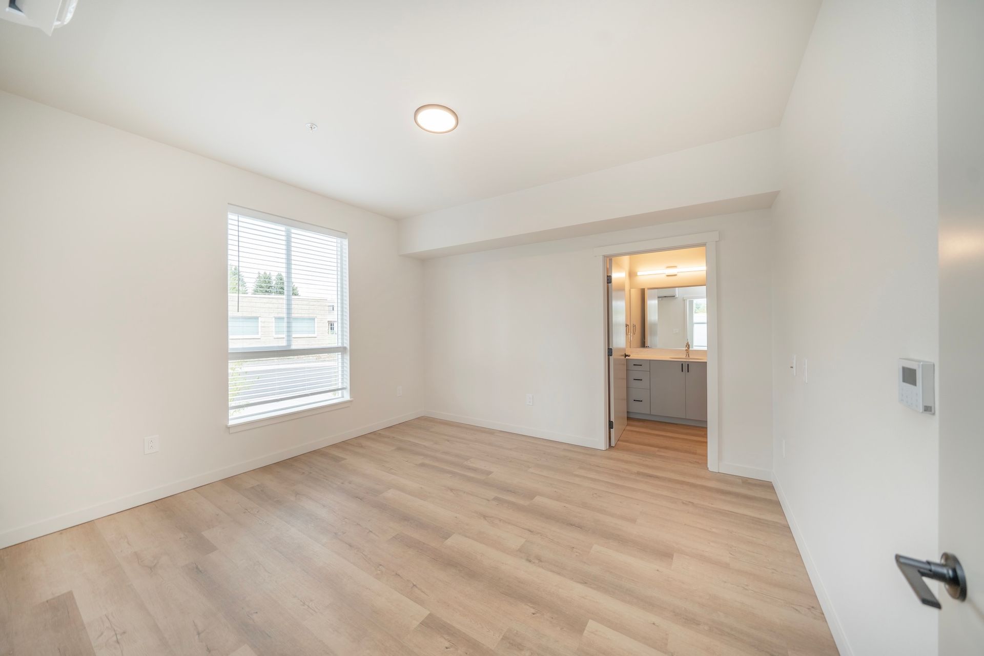 Empty bedroom with light wood floors, white walls, and a bathroom entrance.