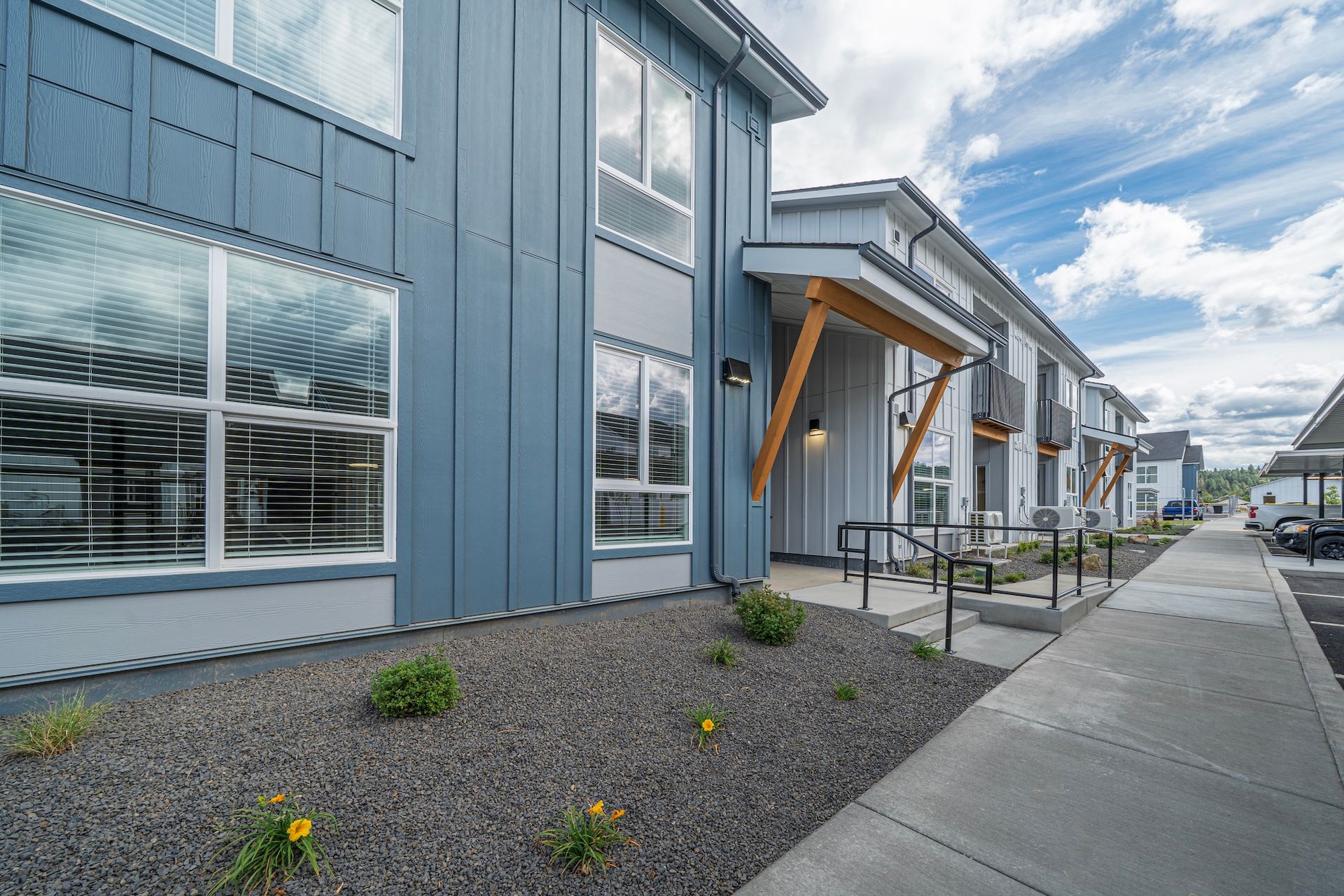 Modern blue townhouses with large windows and a sidewalk, gravel landscaping.