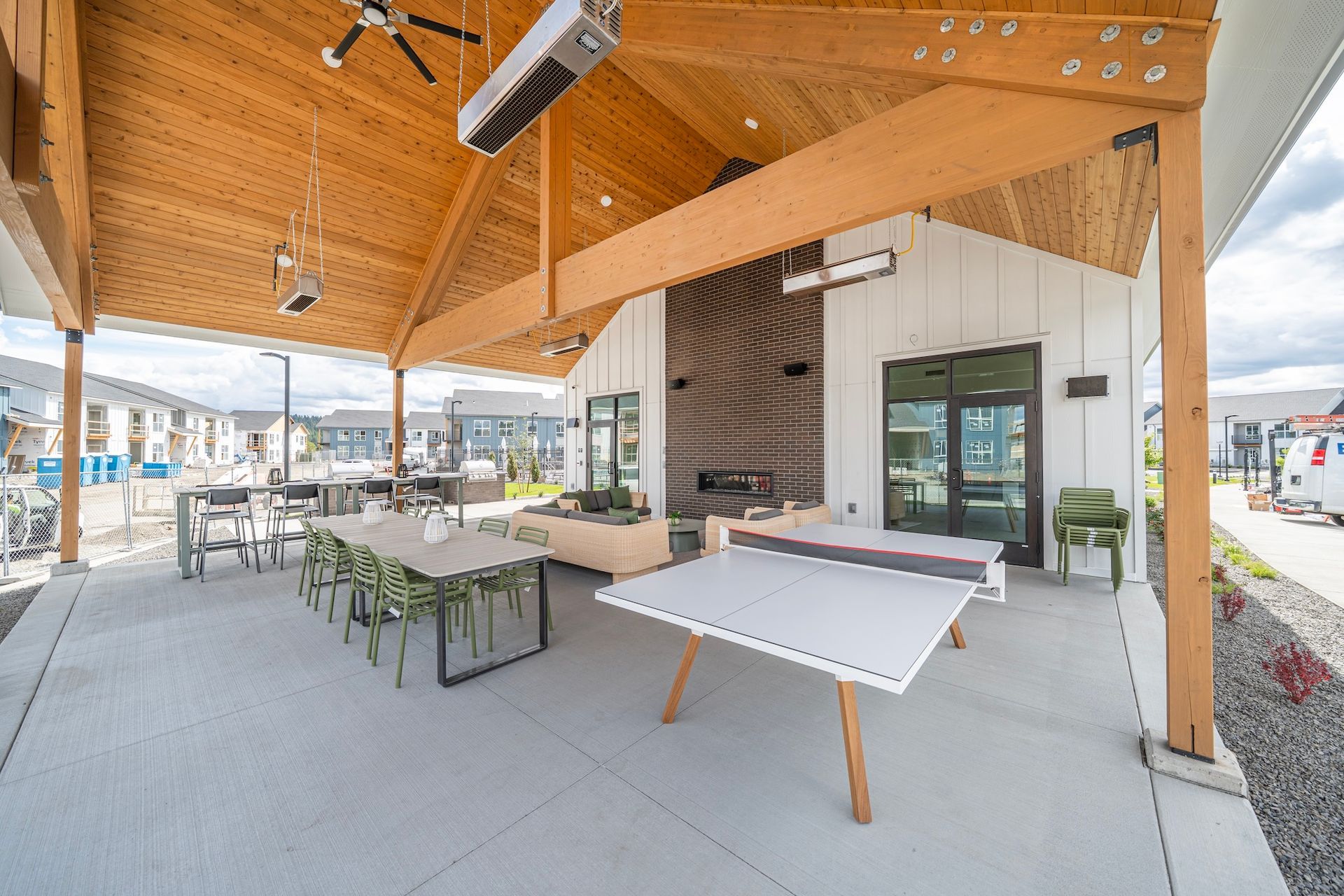 Outdoor covered patio with tables, ping pong, grill, and seating under a wooden ceiling.