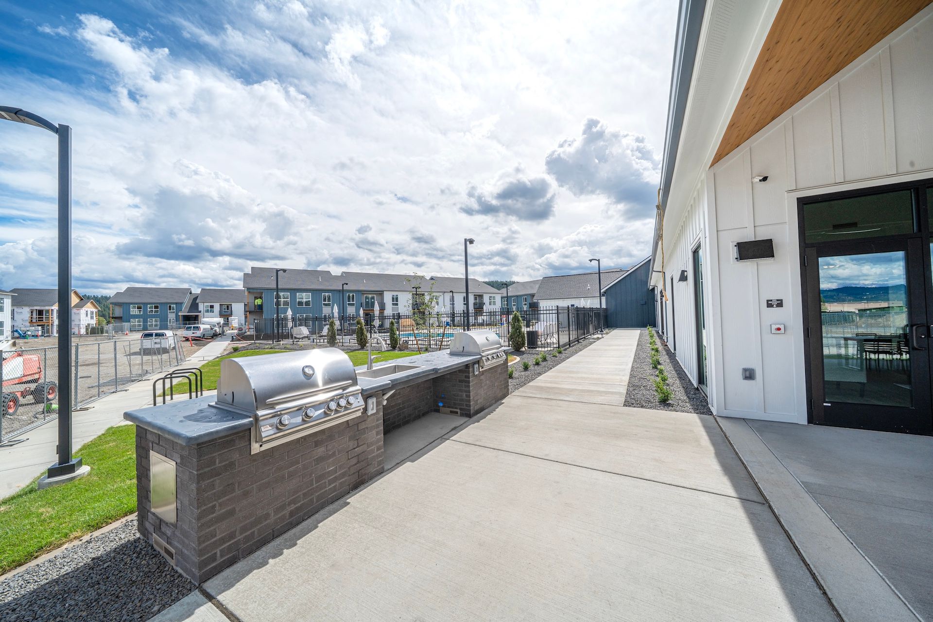 Outdoor grilling area with two built-in grills, next to a modern building, with townhouses in the background.