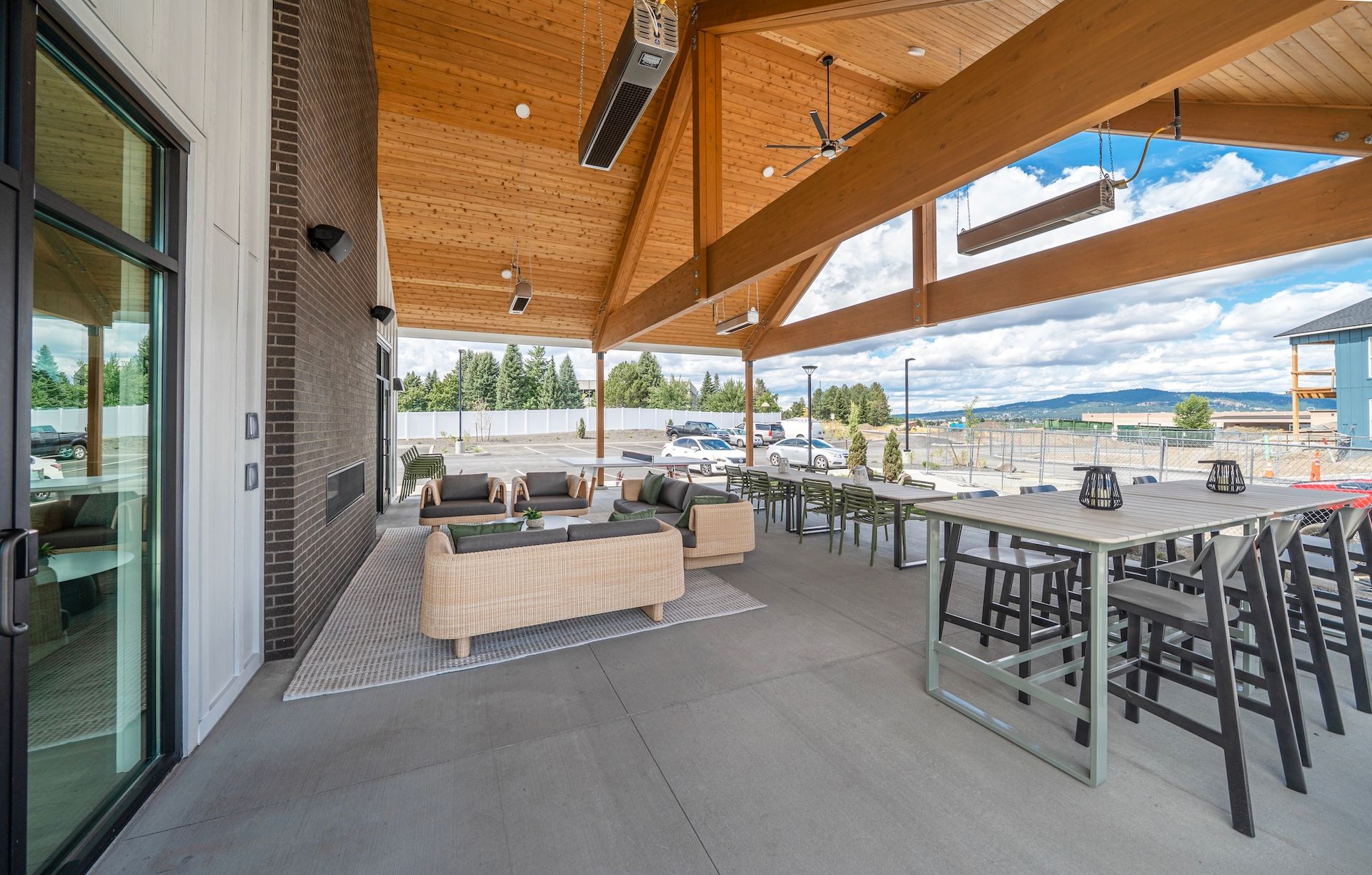 Patio with seating under a wooden roof, tables, and chairs overlooking a distant landscape.