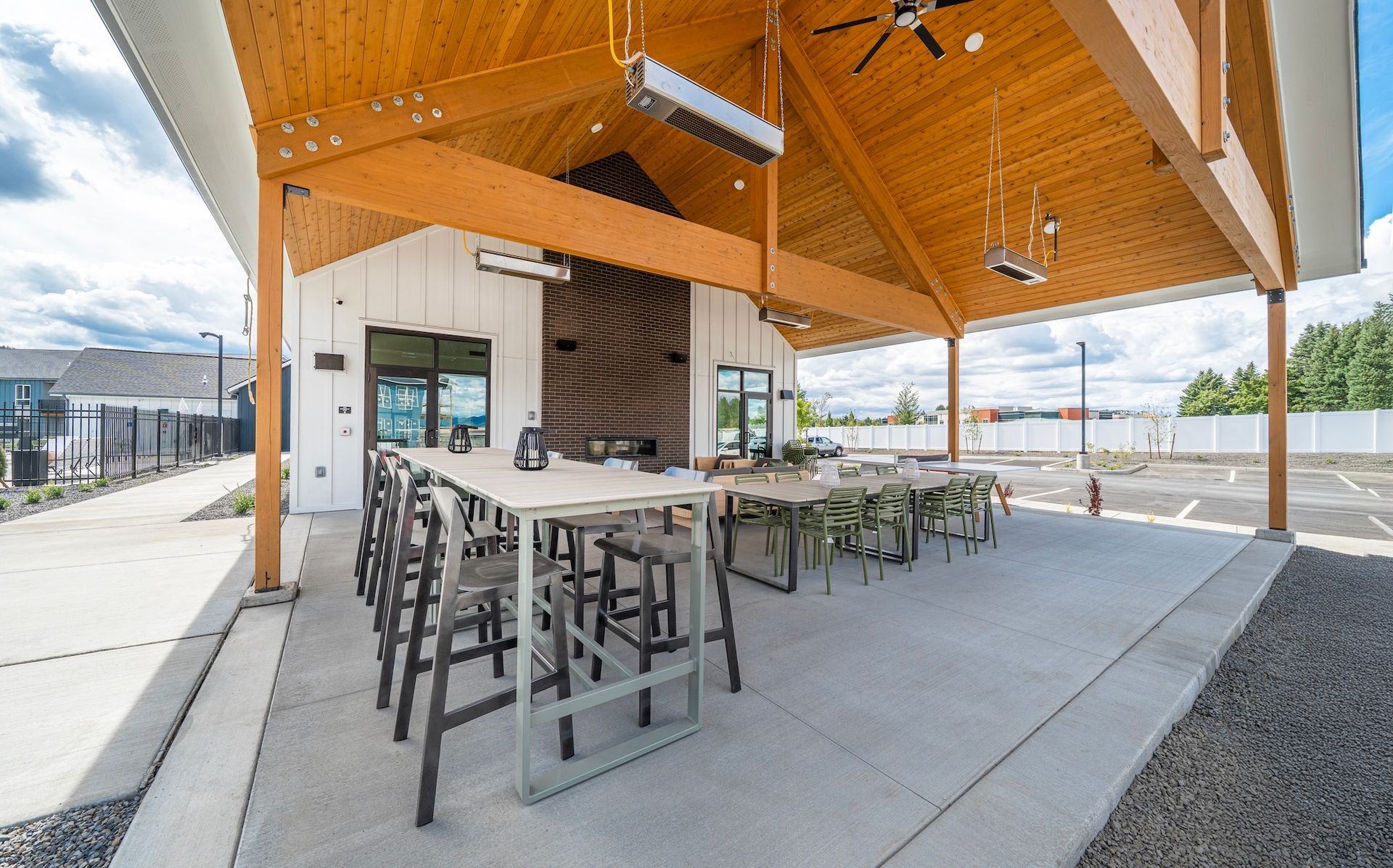 Outdoor covered patio with tables and chairs; white building, wooden ceiling.