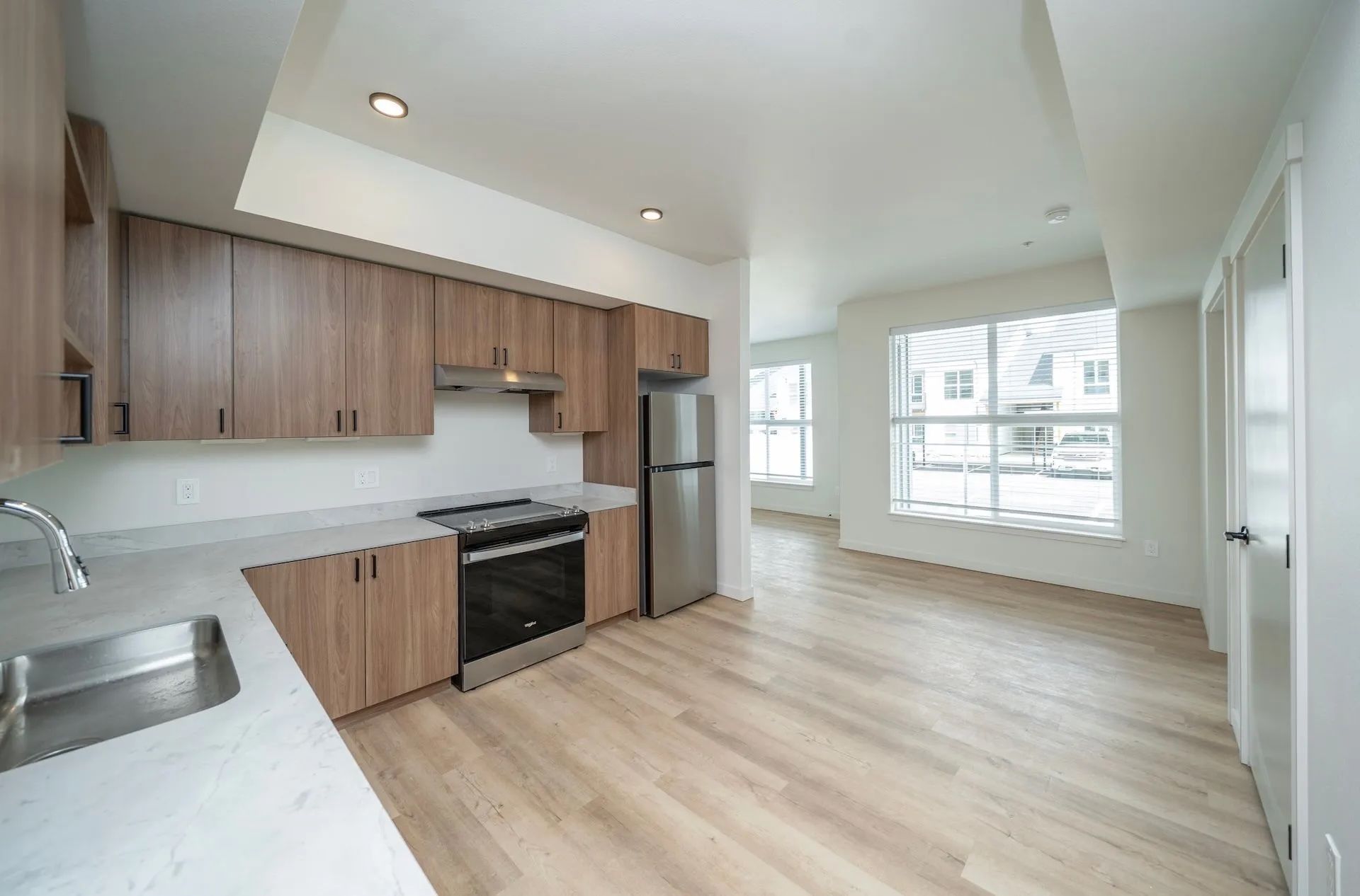 A modern kitchen in a Signal Point apartment in Liberty Lake, Washington, featuring wood-finish cabinetry, stainless steel appliances, under-cabinet lighting, and light wood flooring — appliances are included as a standard amenity.