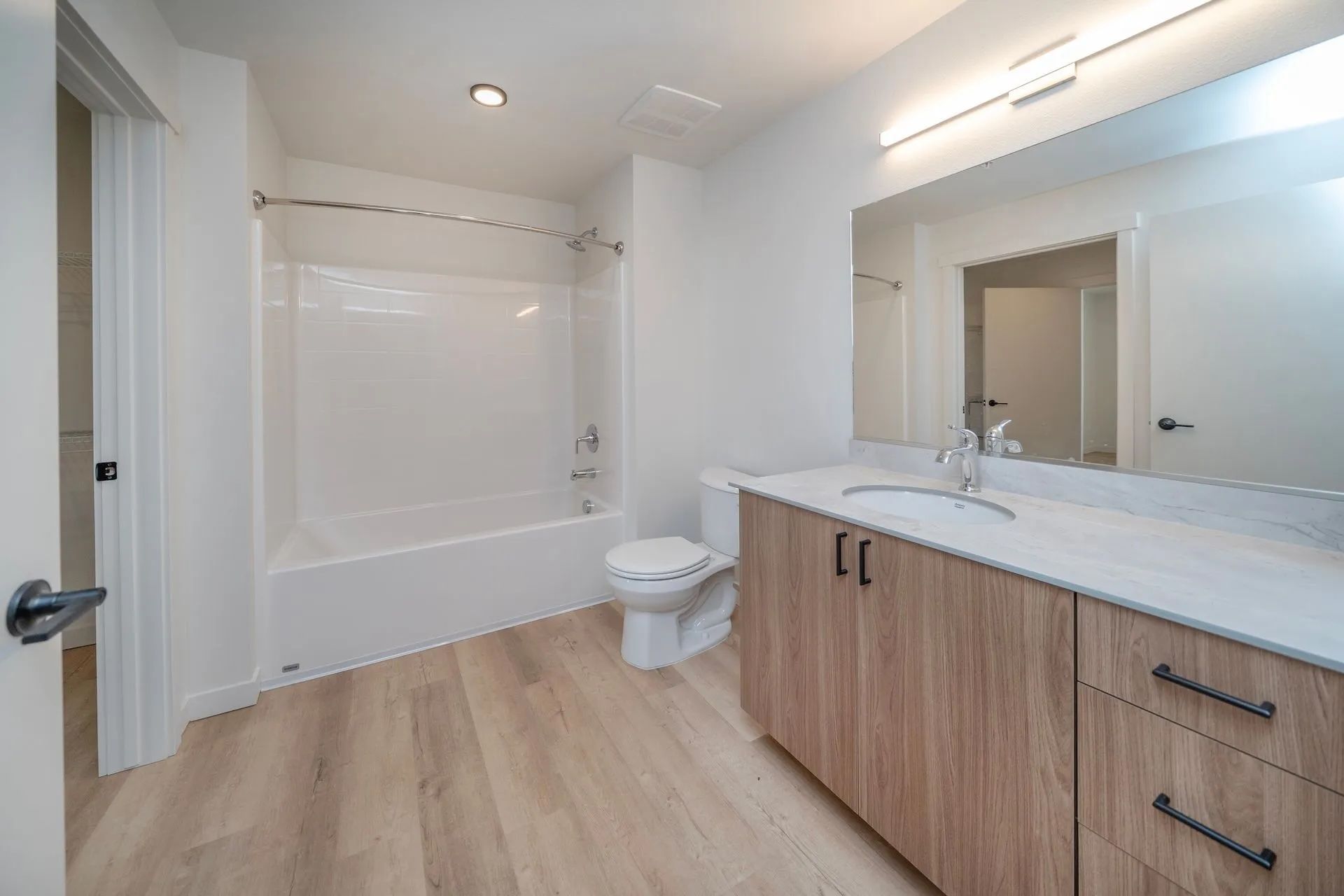 A modern bathroom in a Signal Point apartment in Liberty Lake, WA, with a white tub and toilet, a wood-finish vanity, and light wood flooring — clean, brand-new, and ready for move-in.