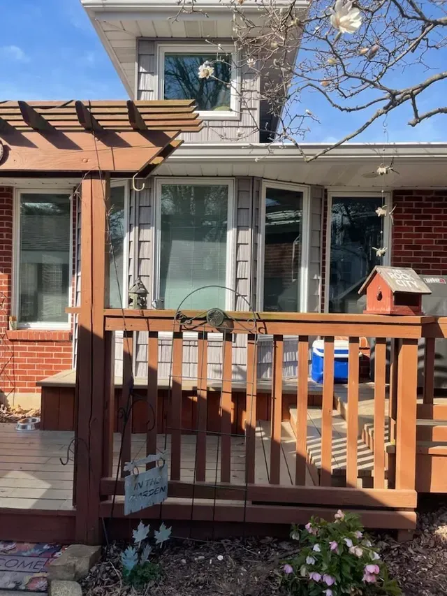 Wooden deck with pergola, leading to a house with windows and siding.