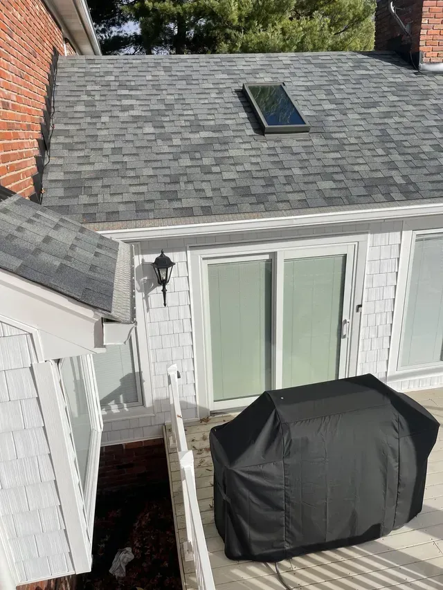 Backyard patio with a covered grill, white French doors, and a gray shingled roof with skylight.