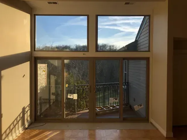 Large windows and sliding glass doors open to a balcony, allowing light into a room with hardwood floors.