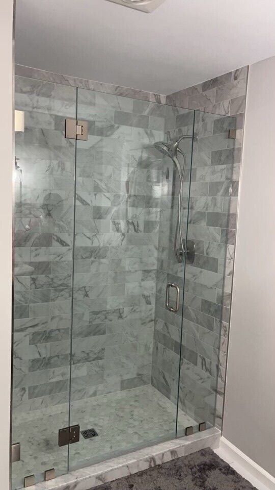 Glass shower with gray marble tile walls and door.