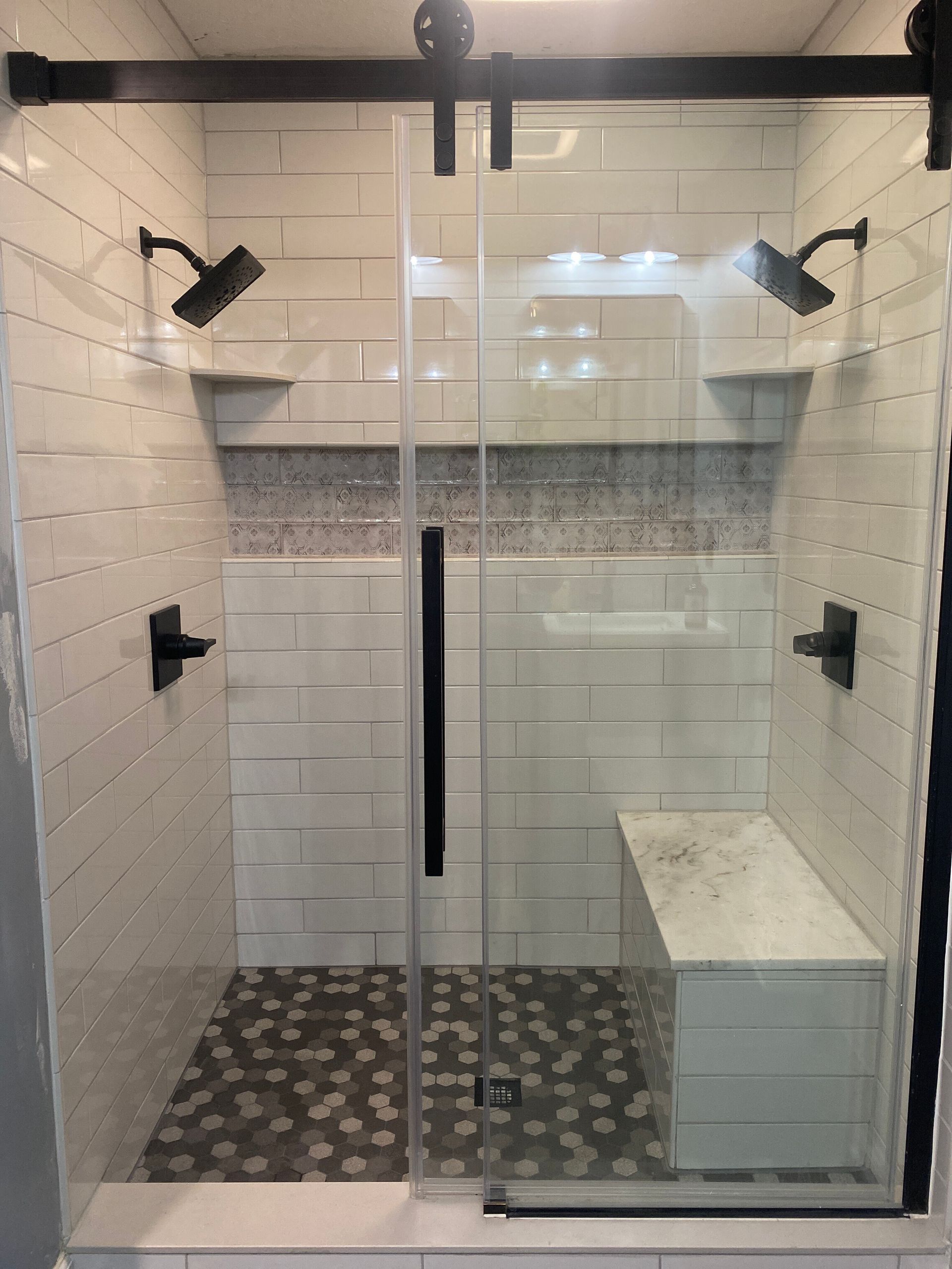 A shower with a sliding glass door and a bench.
