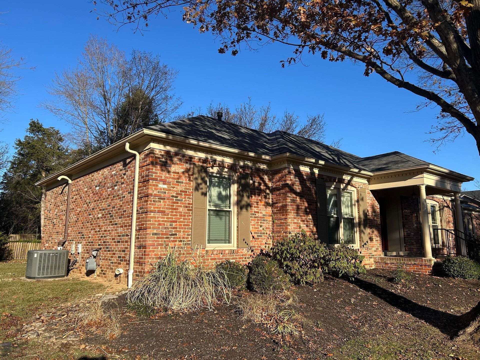 Brick suburban house with a front porch, autumn trees, and a clear blue sky