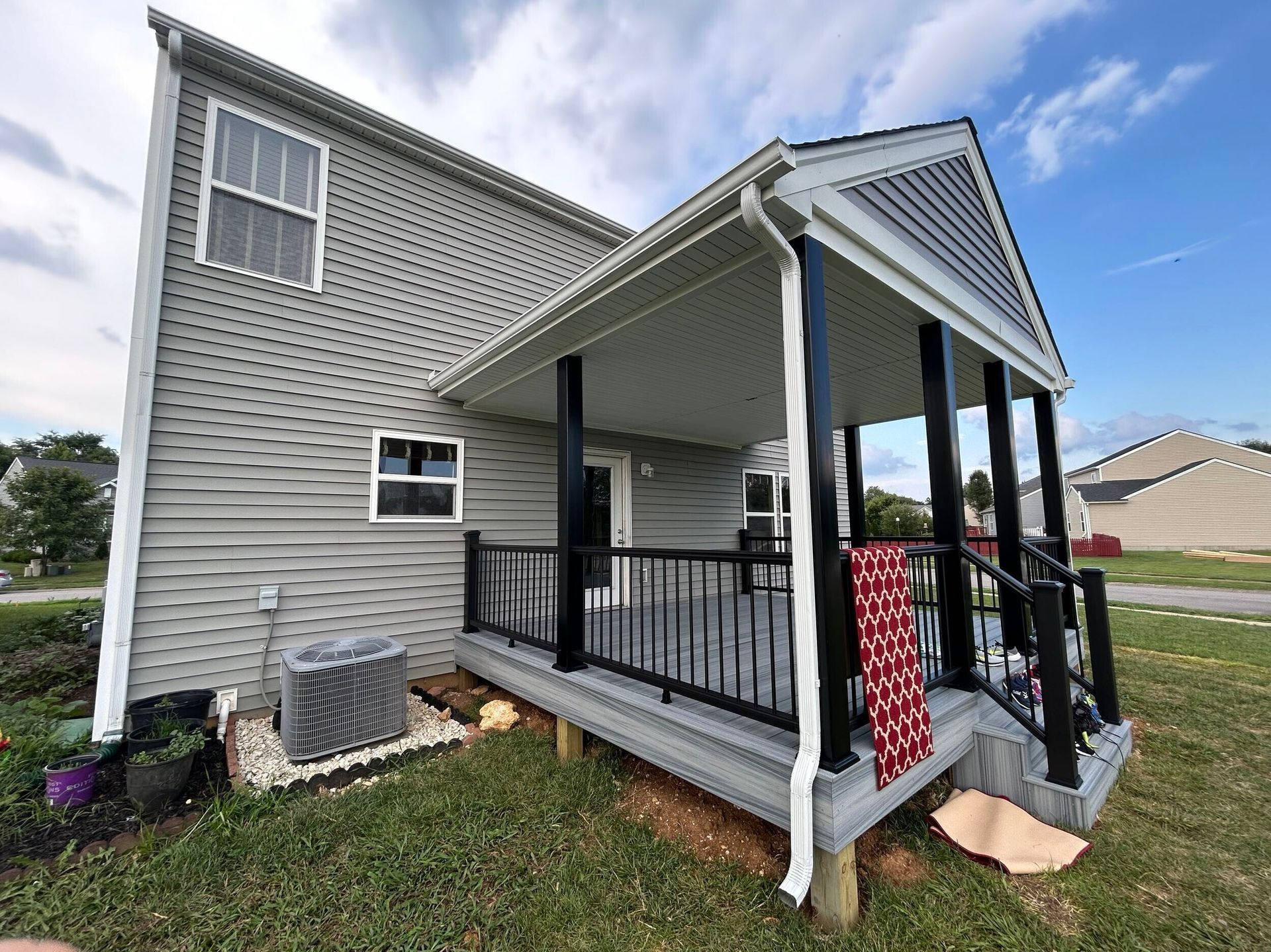Gray house porch with black railings, front steps, and a red blanket draped over the railing
