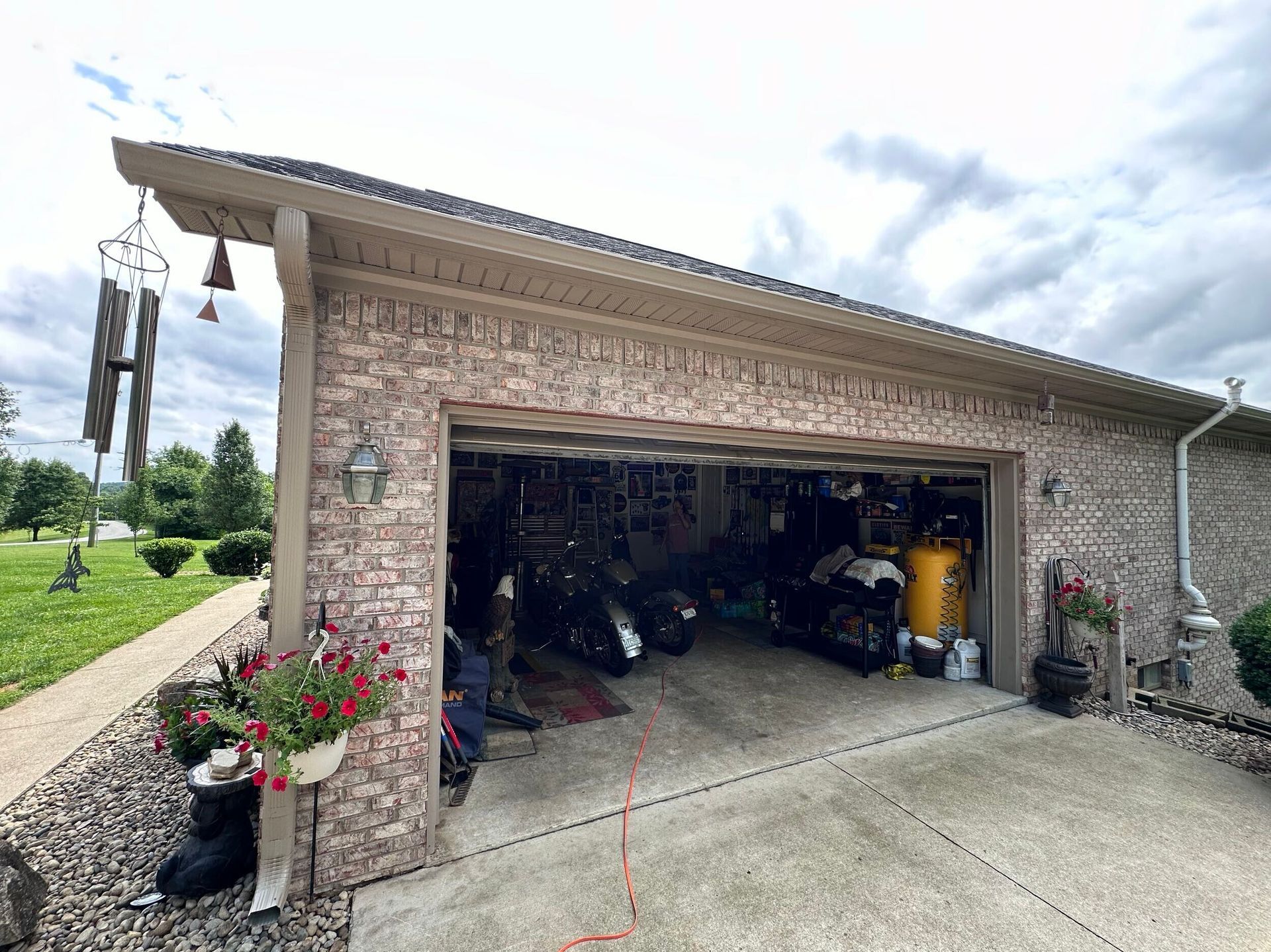 Brick garage with open door, parked vehicles inside, and hanging plants by the driveway