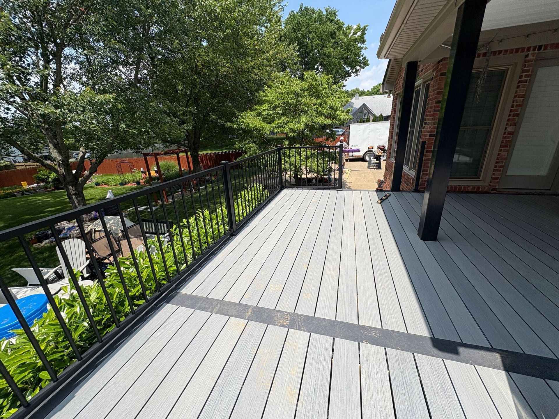 Wooden deck with black railing overlooking a yard with trees and house.