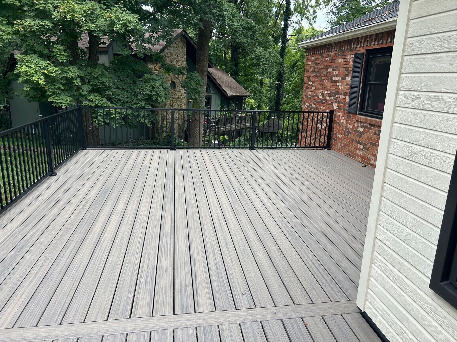 Wooden deck with black railings next to a brick building and a white-sided building with black windows.