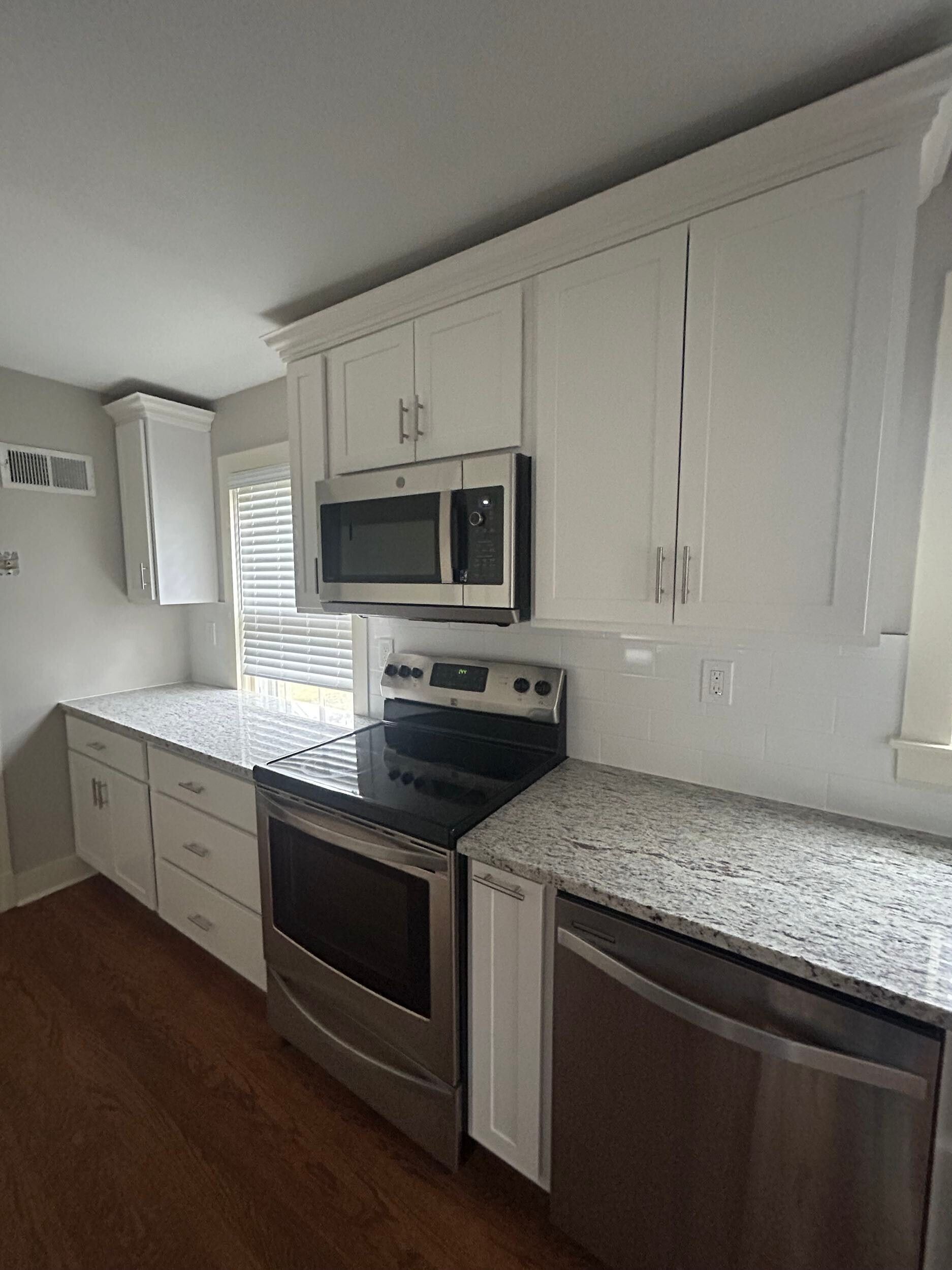 Bright modern kitchen with white cabinets, speckled countertops, stainless steel appliances, and wood floors