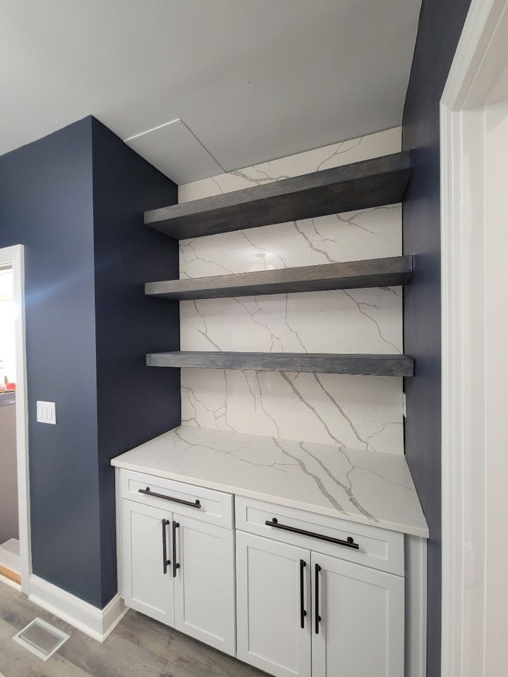 Built-in shelving unit with gray shelves and white cabinets, set against a white marble backsplash, and dark blue walls.