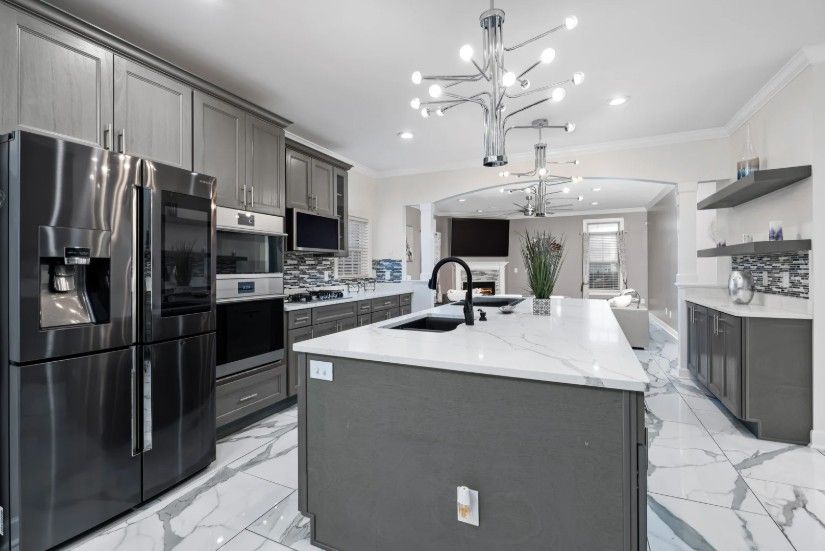 Modern kitchen with dark cabinets, white island countertop, stainless appliances, and chandelier lighting