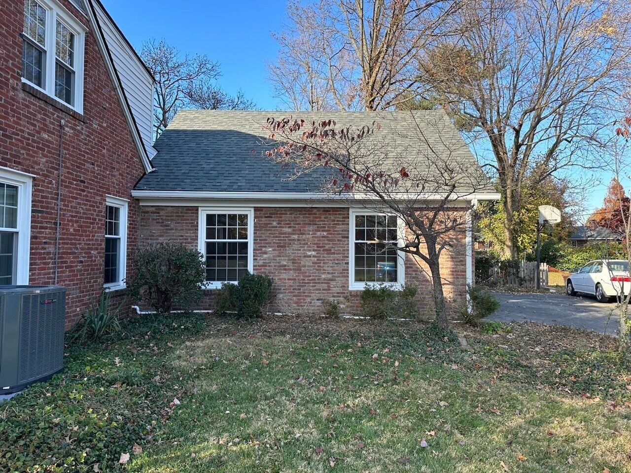 Brick house with white-trim windows, a grassy front yard, and trees under a clear blue sky