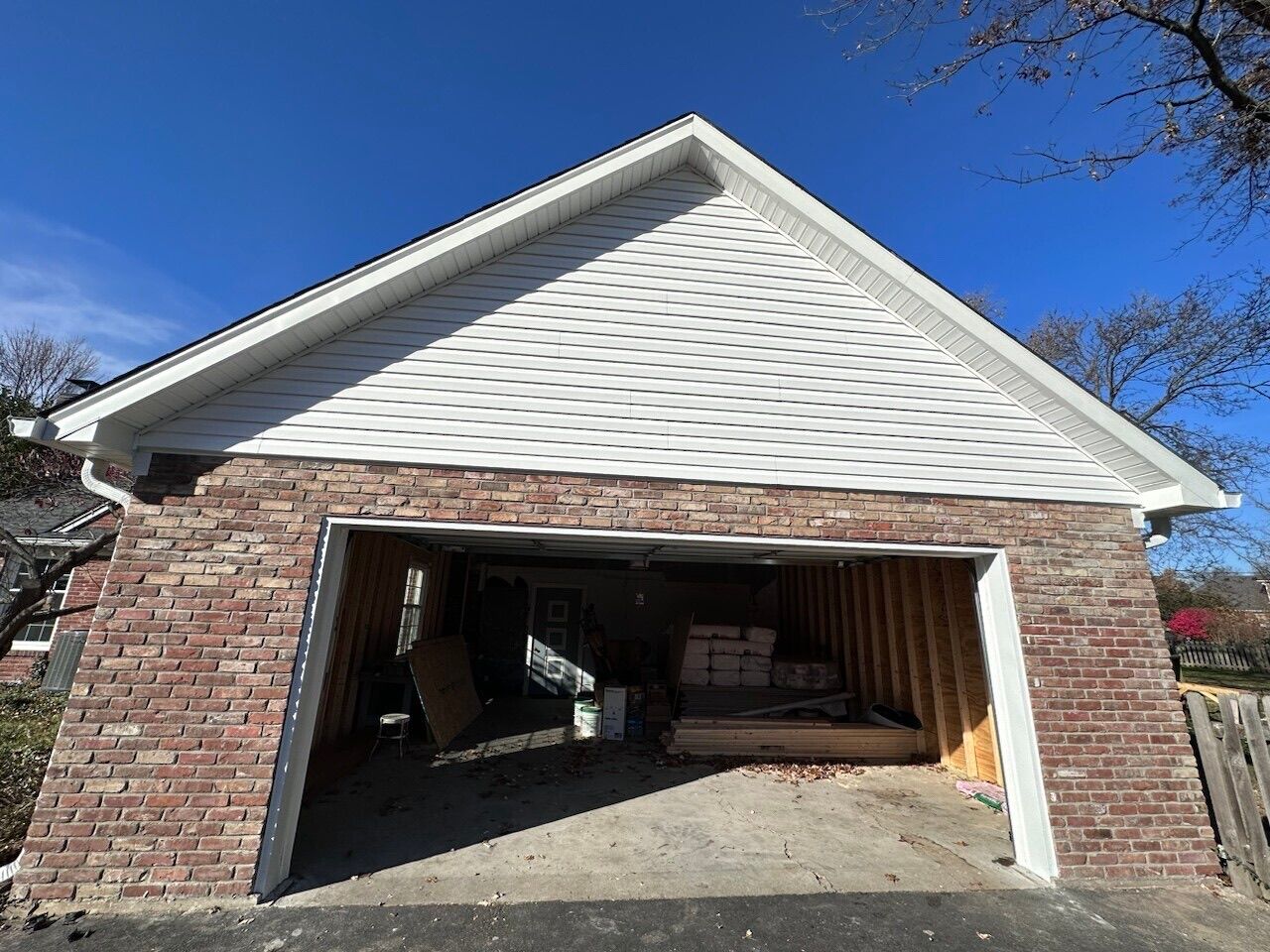 Garage with brick facade, white siding, open door, and blue sky.