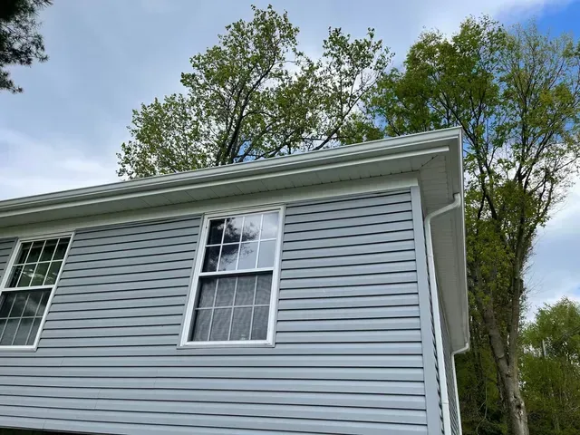 Light gray house siding with white-trimmed windows and trees against a blue sky