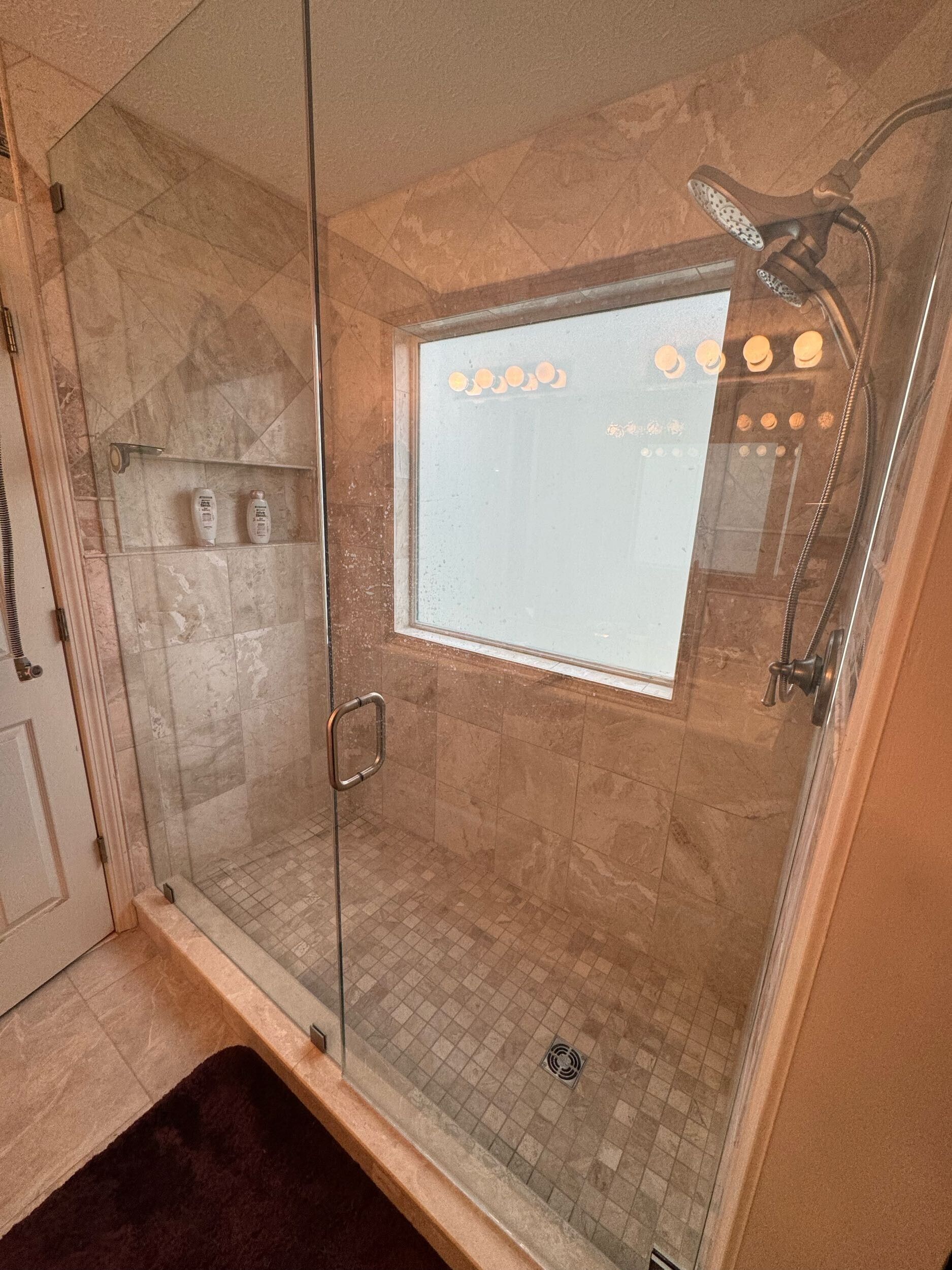 A bathroom with a walk in shower with a glass door and a window.