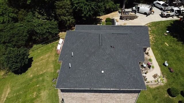 Aerial view of a house with a dark gray shingled roof and surrounding green lawn.
