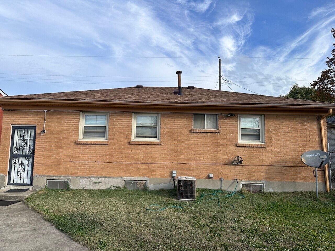 Back of a tan brick house with small windows, a side door, and a satellite dish under a blue sky.