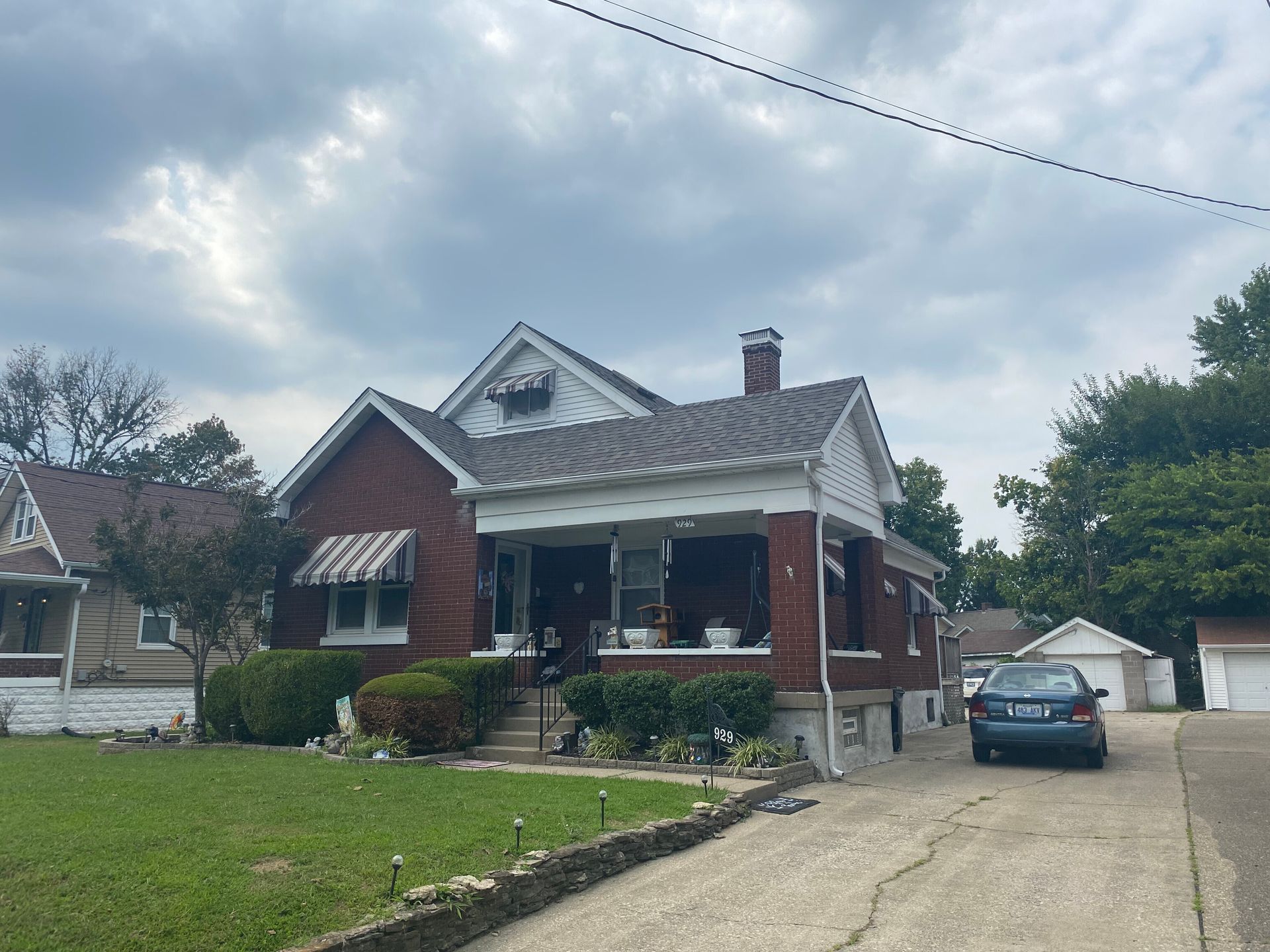 Red brick house with a porch, driveway, and a cloudy sky overhead.