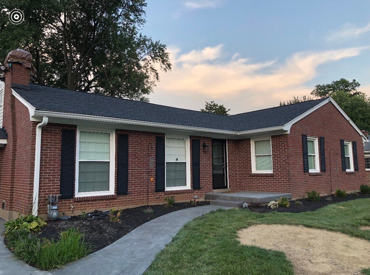 Brick house with black shutters and a new dark roof, front yard with a walkway.
