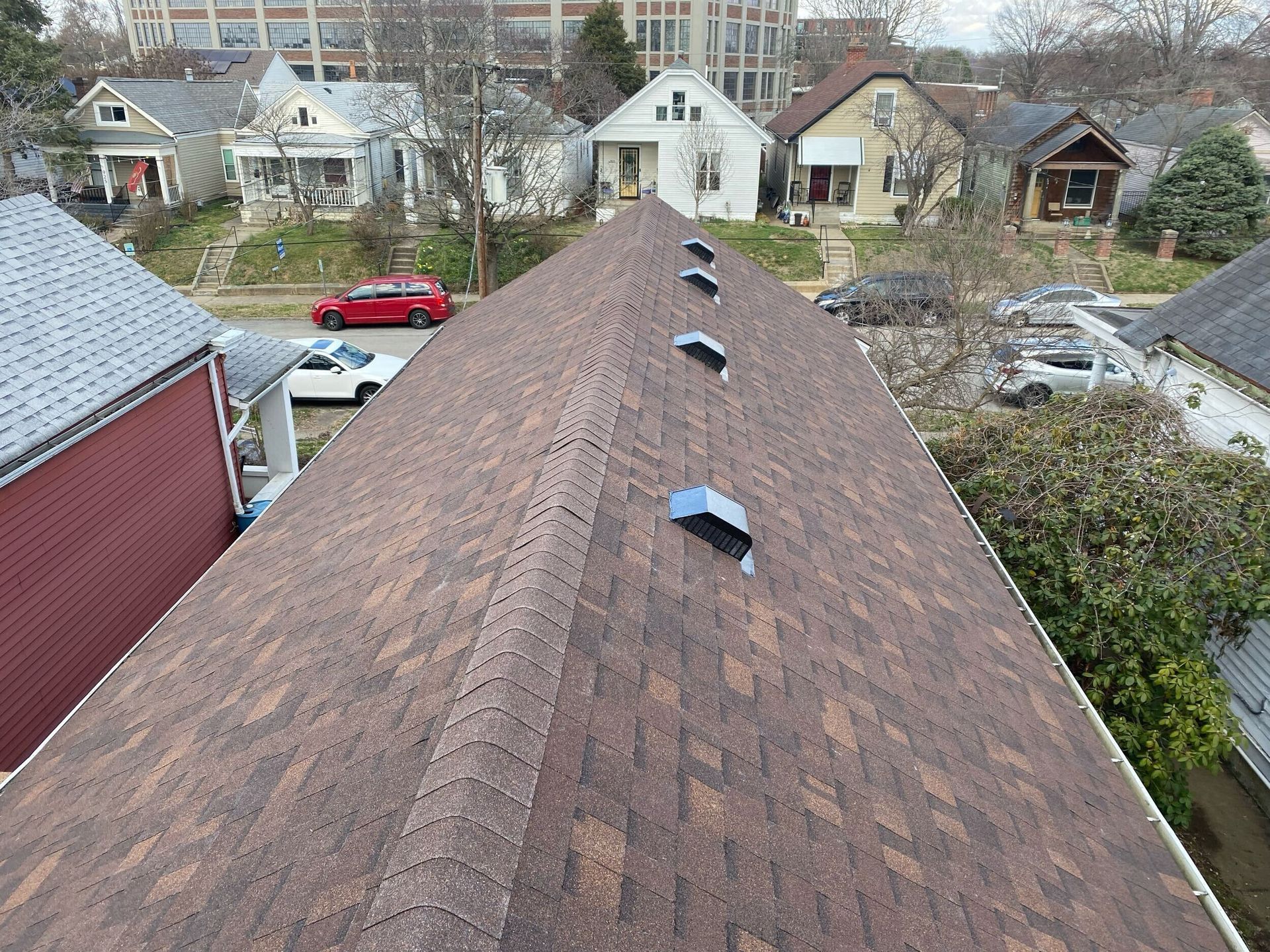 Brown shingle roof with blue vents, viewed from above, houses in the background.
