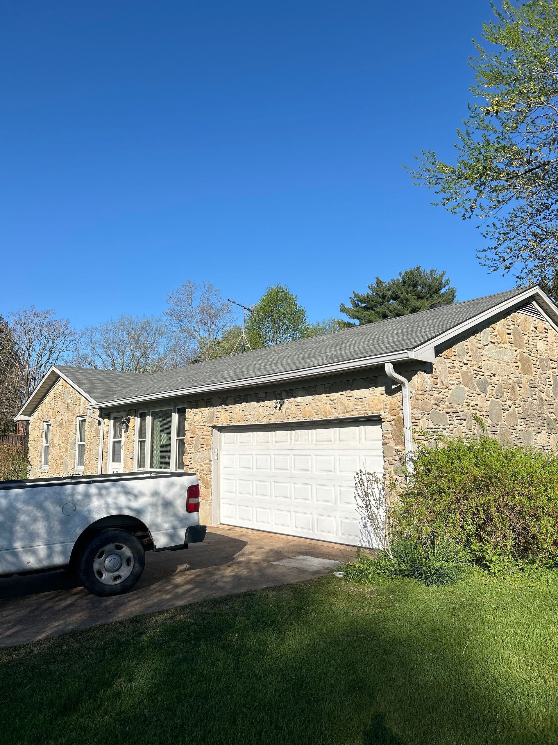 A stone house with a white garage door, a white truck parked in the driveway, and a clear blue sky.