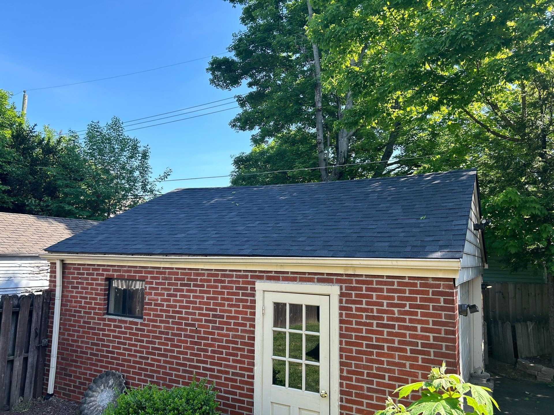 Brick garage with a dark shingled roof and a white door, under a blue sky.