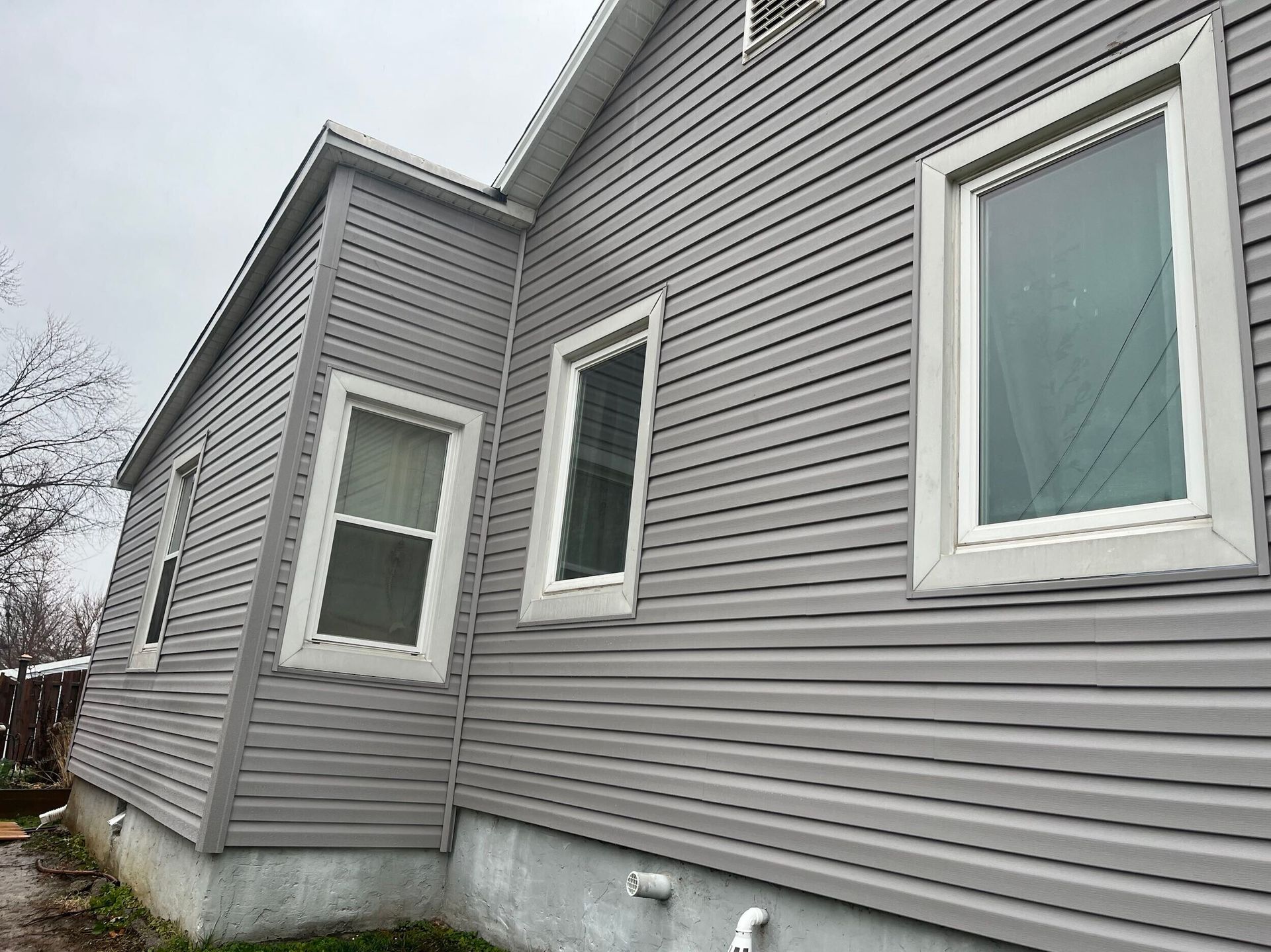 Gray house siding with several windows and a concrete foundation viewed from the side