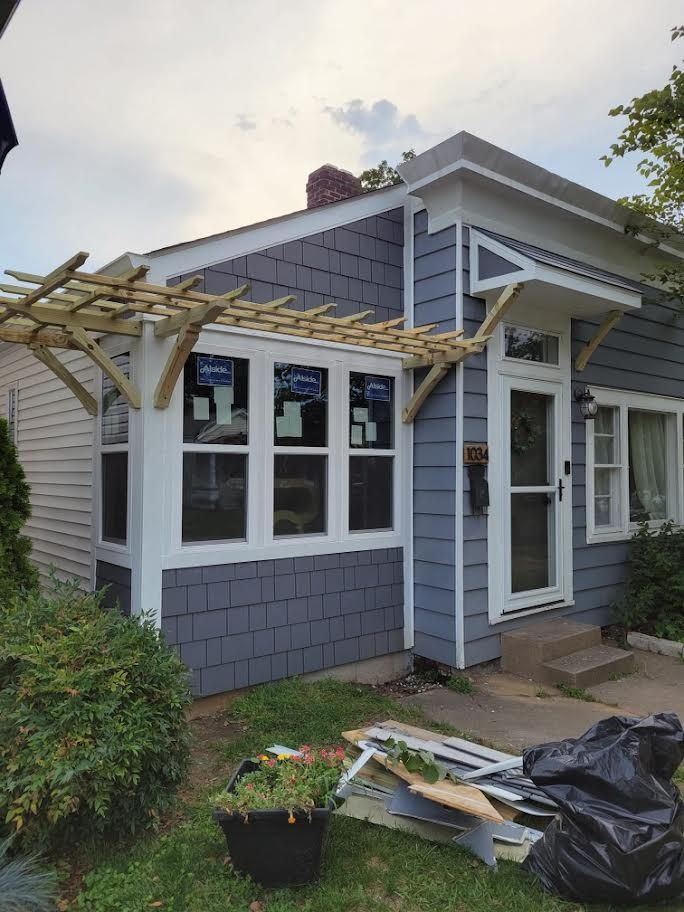 Gray house with white trim and a damaged pergola over the front entry, with debris on the porch and lawn.