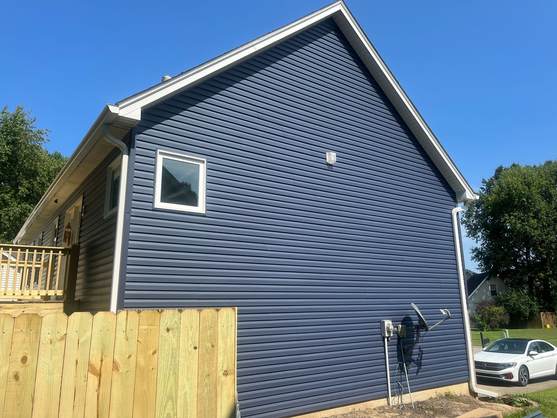 Blue house exterior with white-trim windows, wooden fence, and a car parked beside it under a clear sky