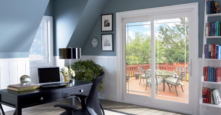 A home office with a desk , chair , computer and sliding glass doors leading to a balcony.