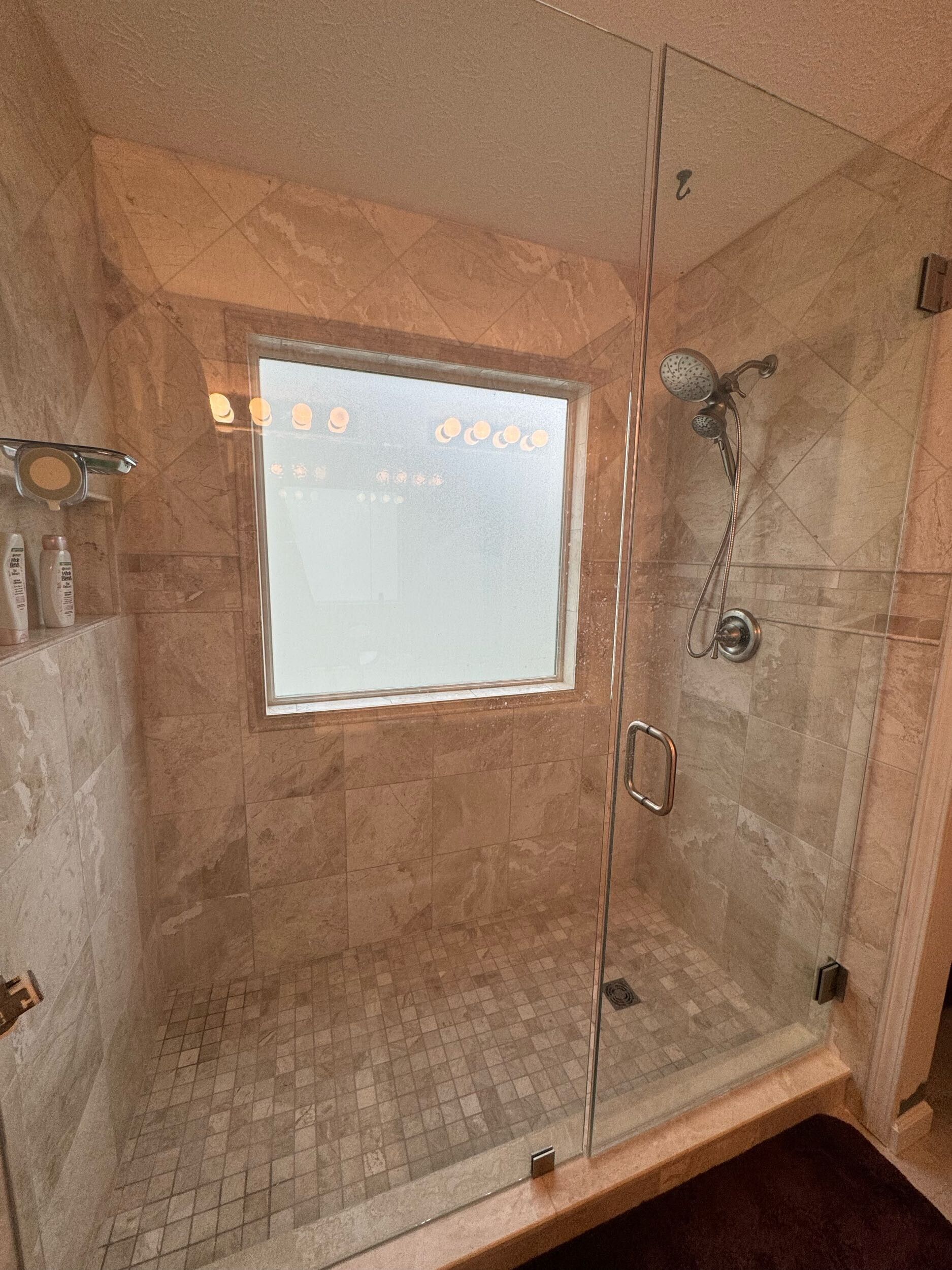 Empty tiled shower with glass door and a small window.