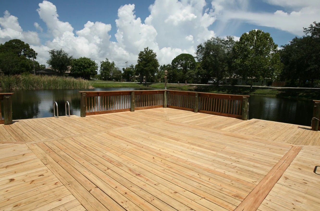 Wooden deck over a pond under a partly cloudy sky, surrounded by trees