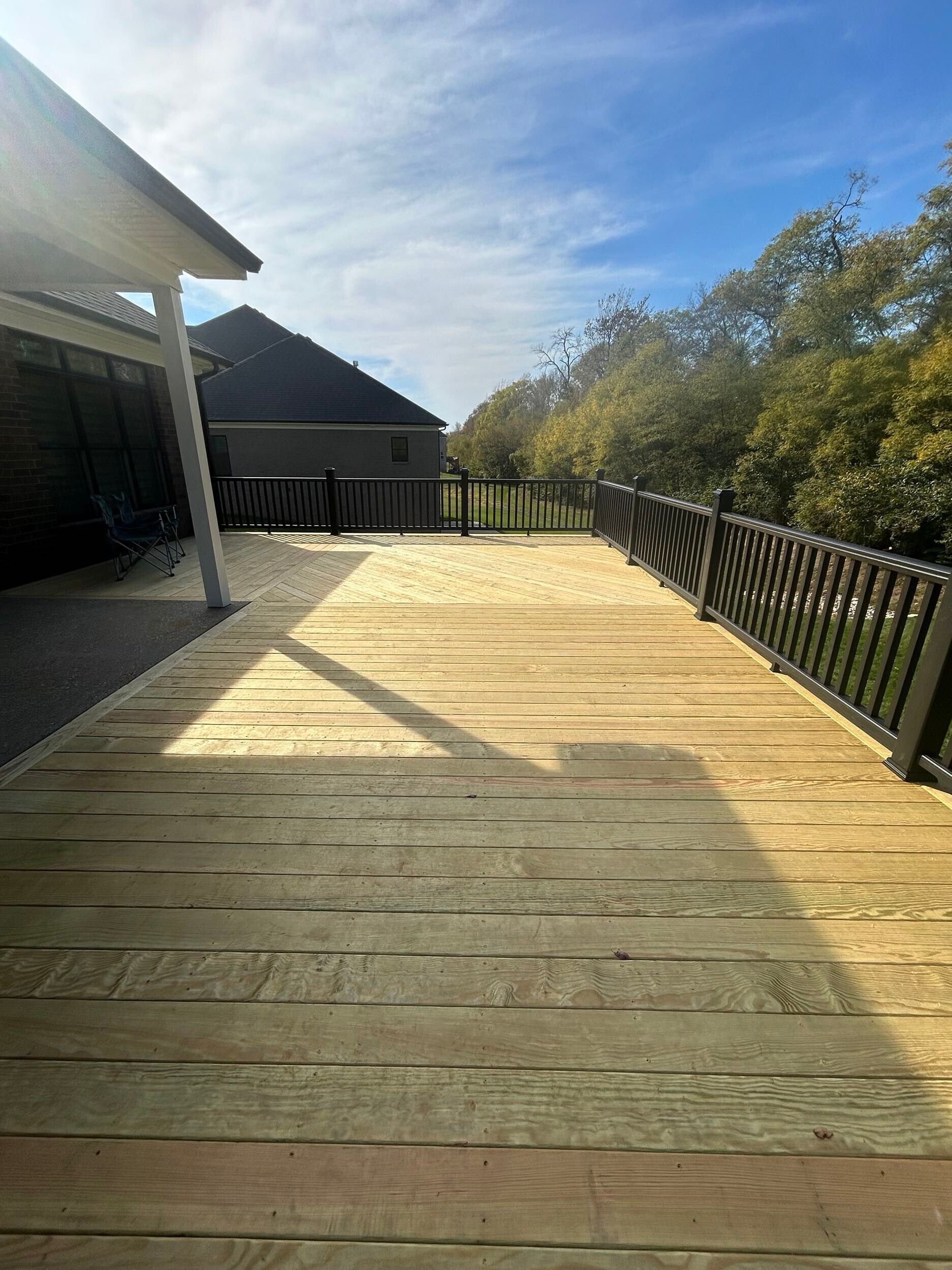 A wooden deck with a metal railing and a house in the background.
