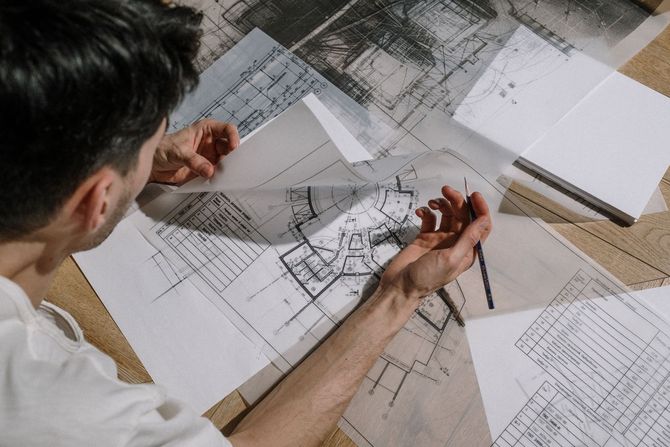Person reviewing architectural blueprints on a desk with a pencil and sketches scattered around