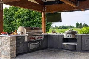 An outdoor kitchen with a grill and a television.