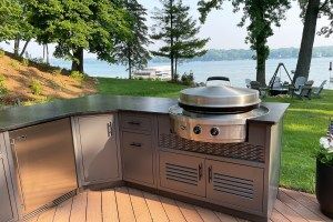 A stainless steel grill is sitting on top of a patio next to a lake.