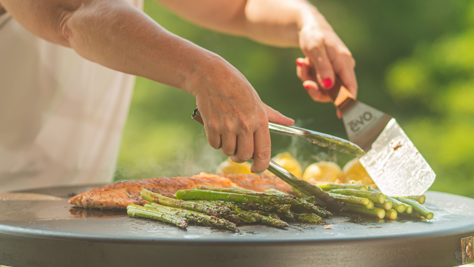 A woman is cooking fish and asparagus on a grill.