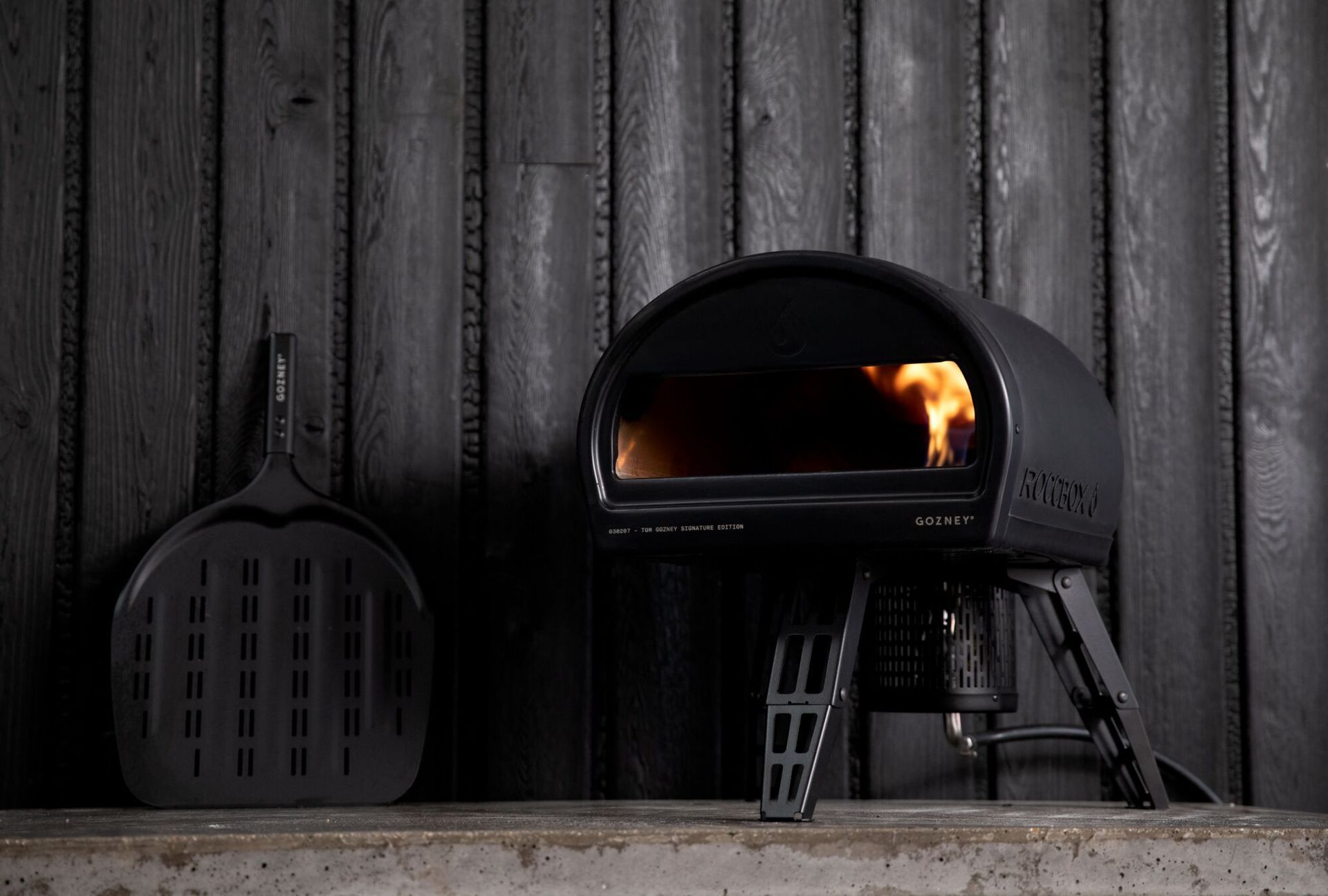 A pizza oven is sitting on a table in front of a black wall.